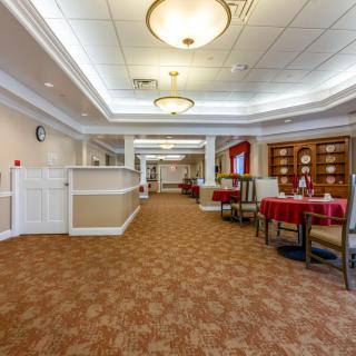 A spacious hallway with carpeted flooring, ceiling lights, and a cozy dining area with tables and chairs.