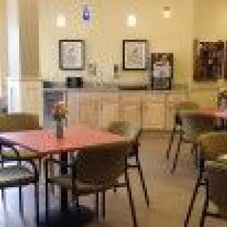 A photograph of a cafeteria with tables, chairs, and a kitchenette in the background.