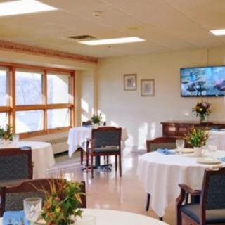 A bright dining area with neatly arranged tables and chairs, featuring large windows and a television.