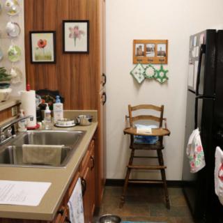 A small, cozy kitchen with a wooden high chair and decorated walls.