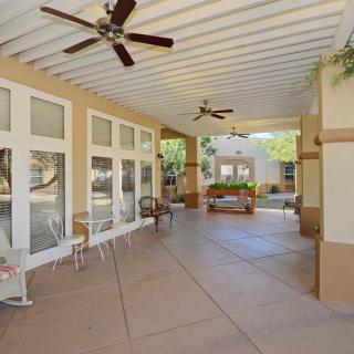 A spacious covered patio featuring ceiling fans, stylish outdoor furniture, and large windows overlooking a garden.