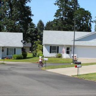 A suburban street with houses, a driveway, and a person riding a bicycle.