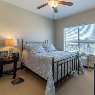 A cozy bedroom with a metal bed frame, nightstand, lamp, and ceiling fan.