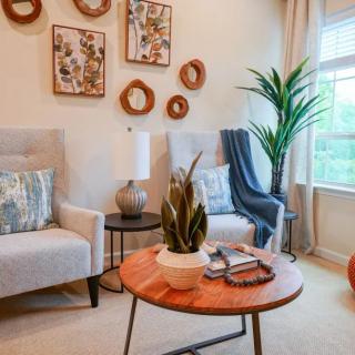 A cozy living room with modern decor, featuring armchairs, a wooden coffee table, and various wall art pieces.