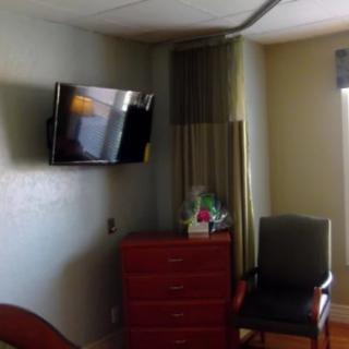A hospital room with a wall-mounted television, dresser, and chair.