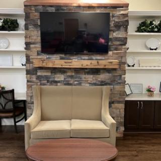 A cozy living room setup featuring a TV mounted above a stone fireplace, with a beige sofa and decorative shelving on either side.