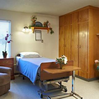 A well-organized hospital room with a bed, medical cart, and wooden furniture.