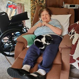 An elderly woman relaxing on a recliner with a black and white cat on her lap.