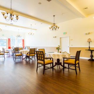 A bright dining room with elegant chandeliers, wooden floors, and neatly arranged tables and chairs.
