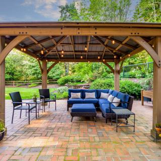 A cozy outdoor patio with a gazebo, featuring comfortable blue seating surrounded by lush greenery.