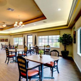 A spacious dining area with multiple tables and chairs, illuminated by natural light from large windows and soft ceiling lights.