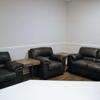 A cozy living room setup with dark leather sofas and small wooden tables against a neutral wall.