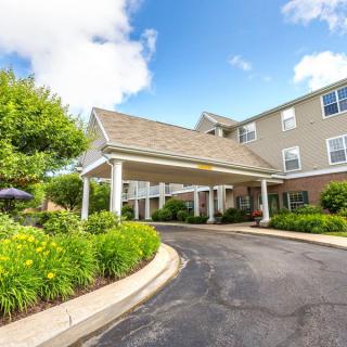 A well-maintained building entrance with a covered driveway and surrounding greenery under a partly cloudy sky.