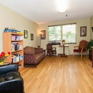 A cozy living room with a sofa, bookshelf, and chairs, featuring a large window for natural light.