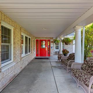 A welcoming front porch with a bright red door, featuring comfortable outdoor seating and decorative plants.