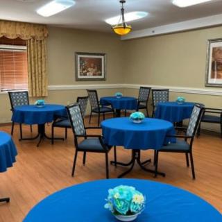 An empty dining room with round tables covered in blue tablecloths, each adorned with a floral centerpiece.