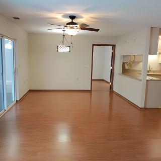 An empty living room with wood flooring and a ceiling fan.