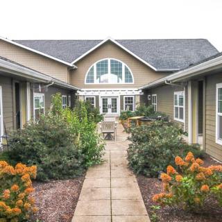 A beautiful garden pathway flanked by blooming flowers leads to a house with large windows.