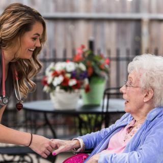 A nurse smiling and interacting with an elderly woman in an outdoor setting.