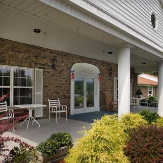 A porch area with chairs and a table, surrounded by decorative plants and supported by columns.