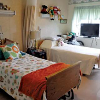 A cozy bedroom with two beds, colorful bedding, and toys on the shelf.