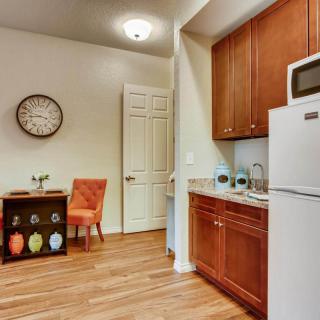 A cozy kitchen with wooden cabinets and flooring, featuring a dining area with an orange chair and decorative elements.