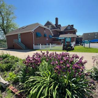 A sunny day showcasing a charming building surrounded by blooming flowers and lush greenery.