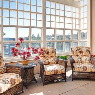 A sunlit room featuring wicker chairs with floral-patterned cushions, surrounded by large windows.