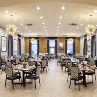 An elegant dining room with neatly arranged tables and chairs, illuminated by chandeliers.