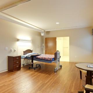 A well-lit hospital patient room featuring a single bed, wooden flooring, and essential furniture.