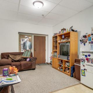 Cozy living room with a couch, entertainment center, television, and fridge adorned with decorations.