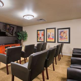 A cozy home theater setup with rows of chairs facing a large screen, decorated with artwork on the walls.
