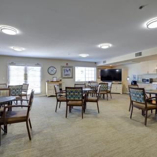 A spacious and well-lit dining room with multiple tables and chairs, featuring a television on the wall.