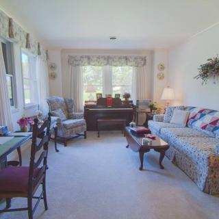 A bright and cozy living room with a sofa, armchairs, and a piano.