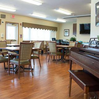 A community space with multiple tables and chairs, featuring a piano in the corner.