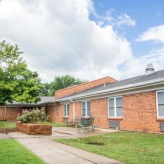 A single-story brick residential building with a yard and cloudy sky.