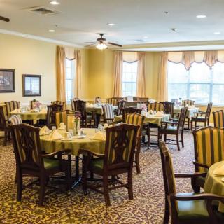 A spacious dining room with neatly arranged tables and chairs, featuring large windows and warm decor.