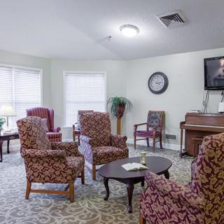 A cozy living room with patterned armchairs, a piano, and a television.