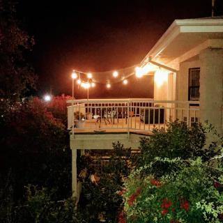 A cozy outdoor deck illuminated by string lights at night, surrounded by lush garden greenery.