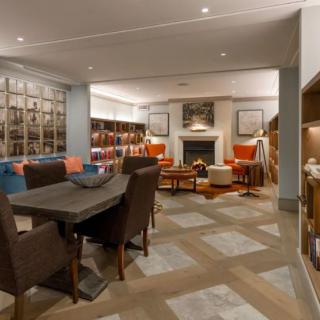 A cozy library interior with bookshelves and comfortable seating around a fireplace.