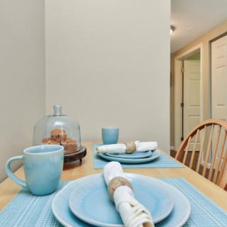 A cozy dining area with a wooden table set with blue dishes, mugs, and neatly rolled napkins.