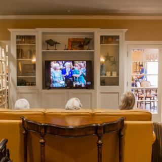A cozy living room where people are sitting on a sofa, watching television.