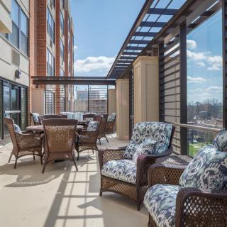 A spacious outdoor balcony with comfortable seating and a table, offering a sunny urban view.