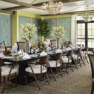 An elegant dining room with a large table set for a formal gathering, featuring flower arrangements and a chandelier.