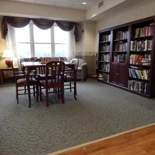 A cozy library space with bookshelves, a table and chairs, and natural light from a large window.