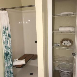 A bathroom featuring a shower with a curtain and adjacent shelving stocked with towels and toiletries.