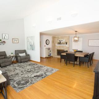 A modern open-concept living and dining area with hardwood flooring, featuring recliner chairs, a patterned rug, and a stylish dining set.