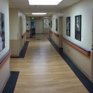 A hospital hallway with wooden flooring and bright overhead lighting.
