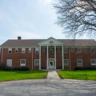 A charming brick building with a classic design, set against a clear sky and manicured lawn.