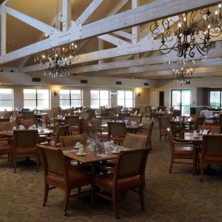 A spacious restaurant dining room with multiple tables and elegant chandeliers.